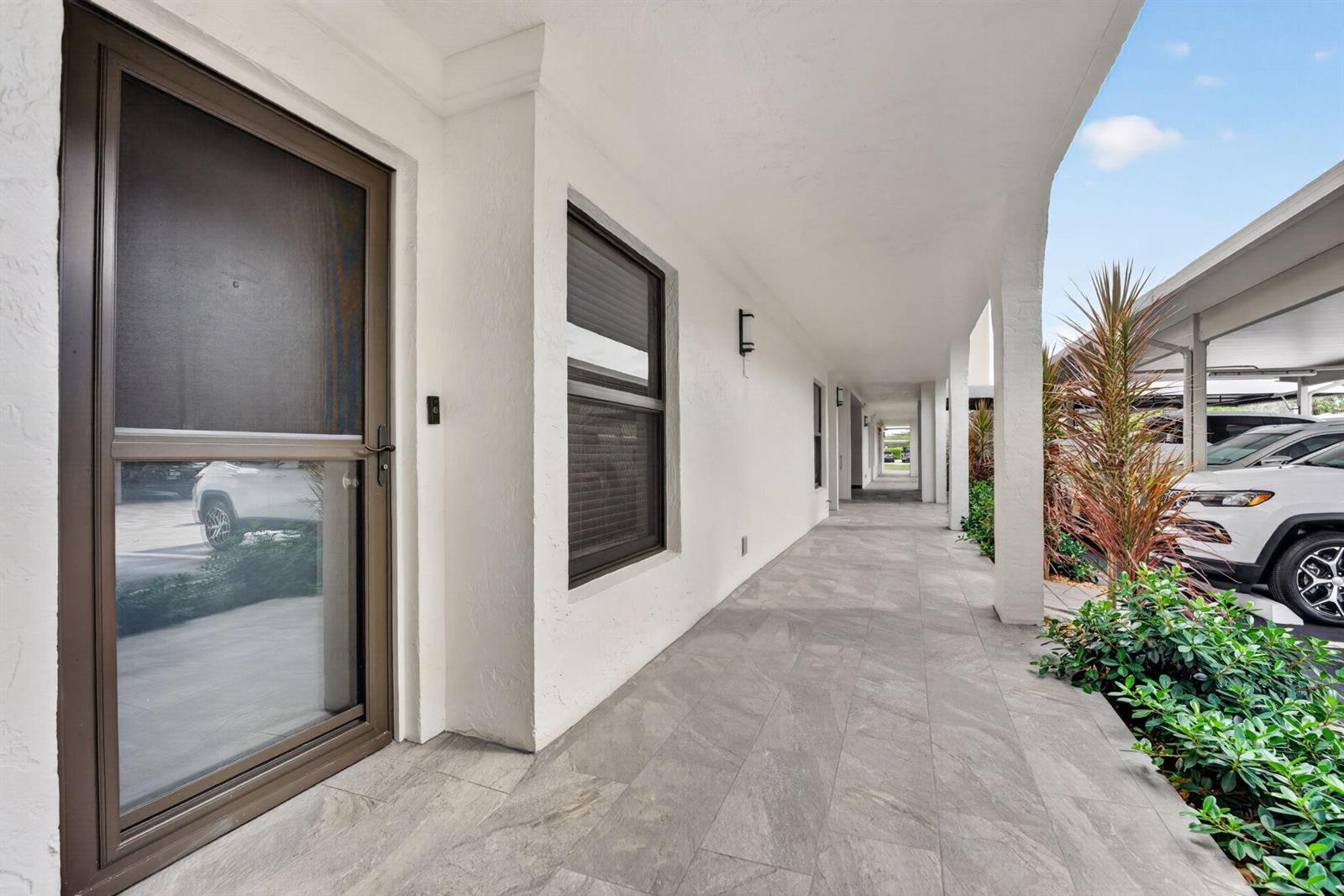 A covered outdoor walkway features light gray tiled flooring, white walls, and a brown screen door — 1627 Riverview Road # 110, Deerfield Beach FL 33441, DEERFIELD BEACH, FL