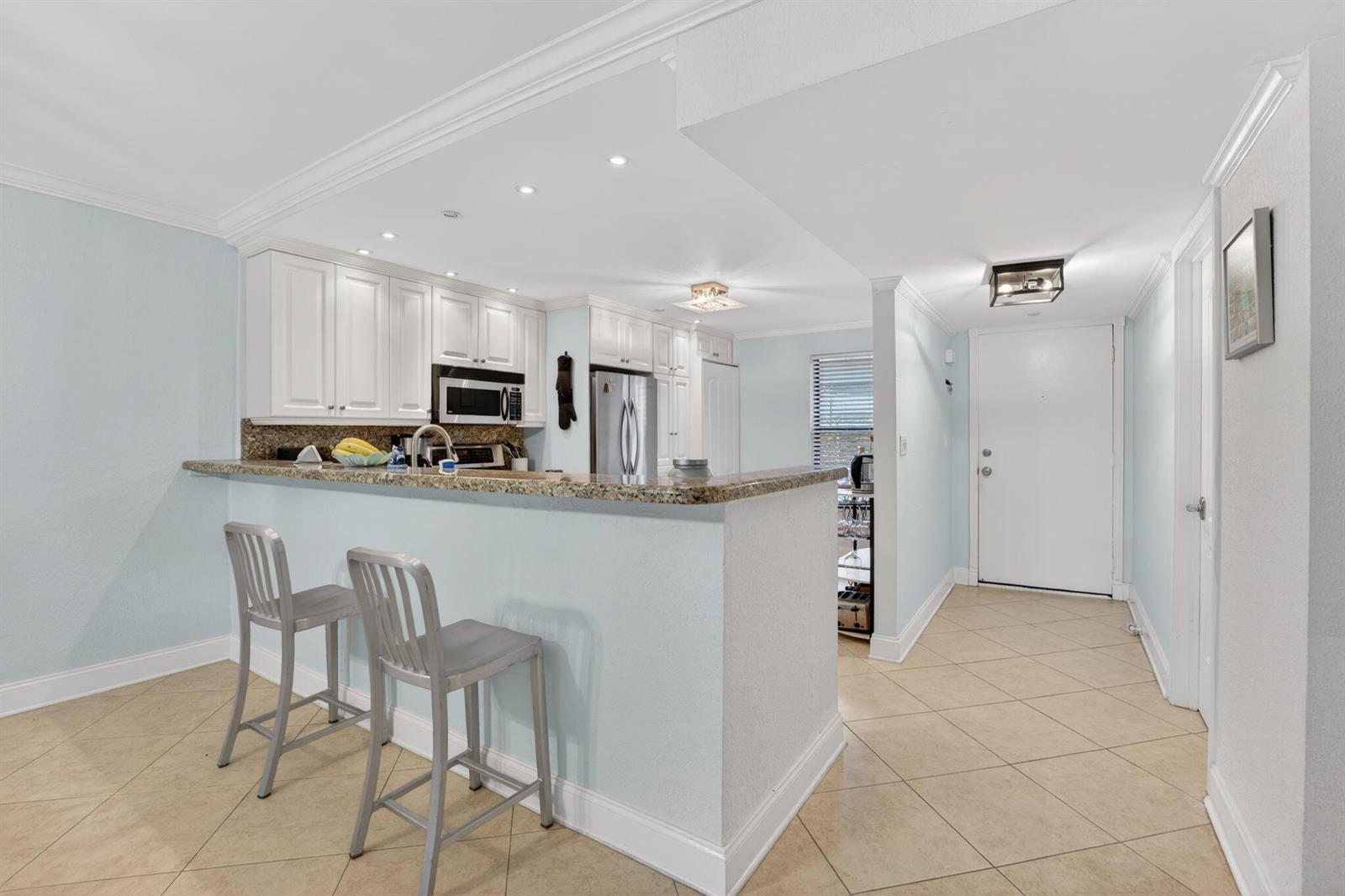 A kitchen with white cabinets, granite countertops, and a breakfast bar with two metal stools — 1627 Riverview Road # 110, Deerfield Beach FL 33441, DEERFIELD BEACH, FL