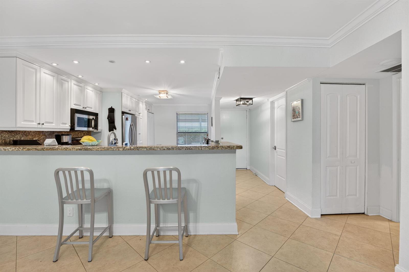 A kitchen with white cabinets, granite countertops, and a breakfast bar with two metal stools — 1627 Riverview Road # 110, Deerfield Beach FL 33441, DEERFIELD BEACH, FL
