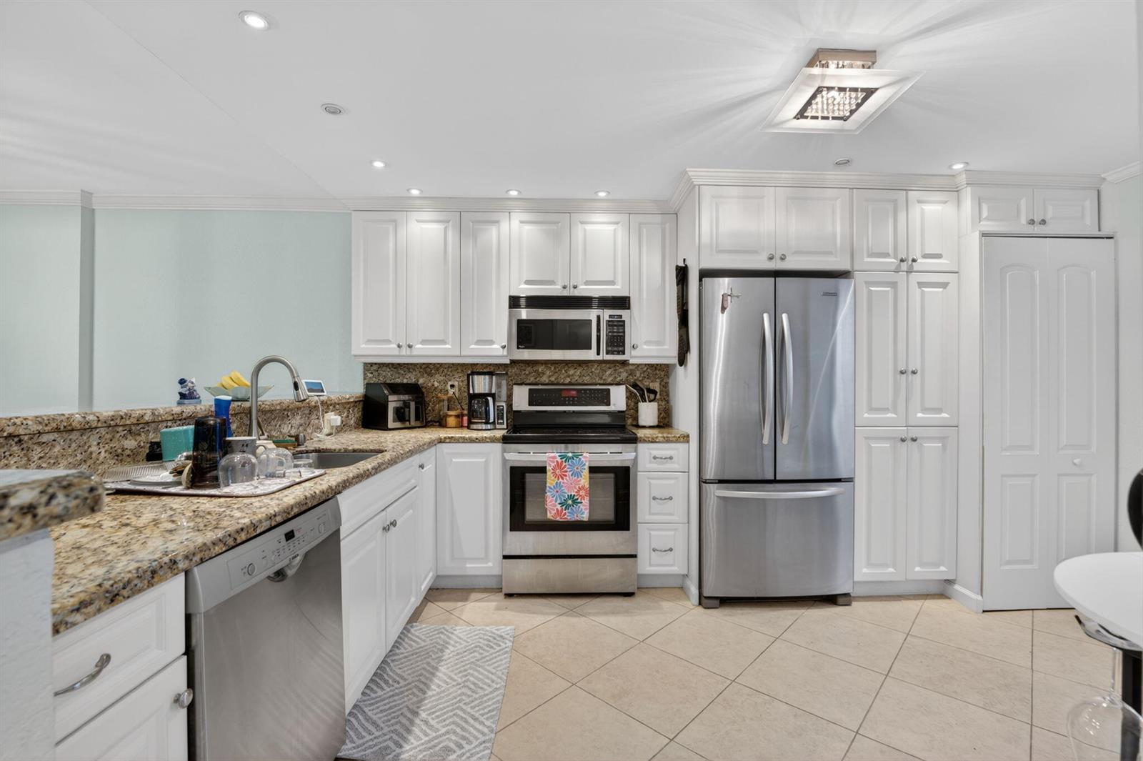 A kitchen features white cabinetry, granite countertops, stainless steel appliances, and light-colored tile flooring — 1627 Riverview Road # 110, Deerfield Beach FL 33441, DEERFIELD BEACH, FL