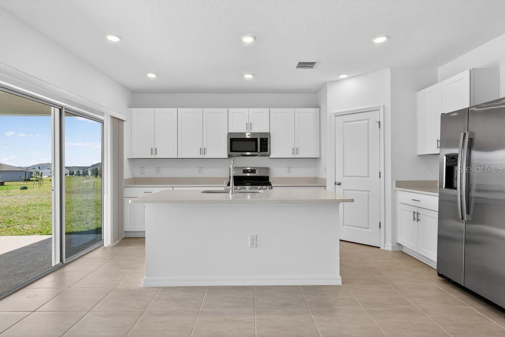 A modern kitchen features white cabinetry, stainless steel appliances, a center island, and tile flooring — 217 STREAMWATER WAY, GROVELAND, FL