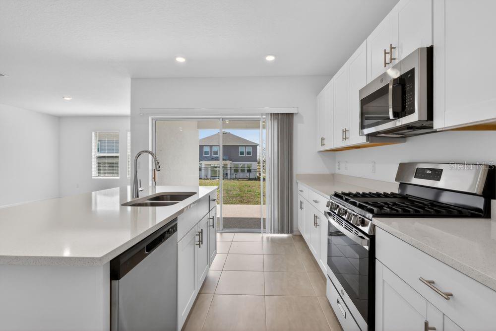 A modern kitchen features white cabinetry, quartz countertops, stainless steel appliances, and a sliding glass door — 217 STREAMWATER WAY, GROVELAND, FL
