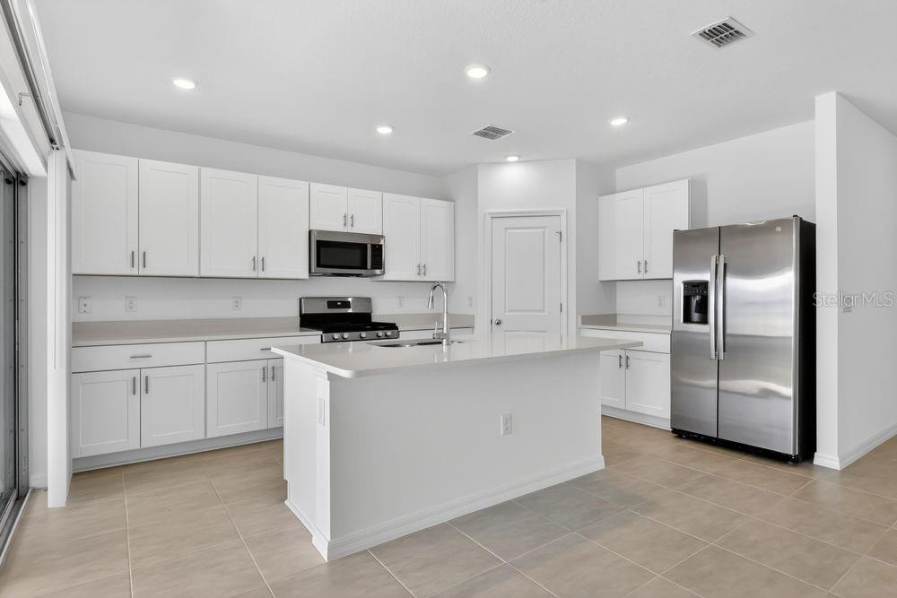 A modern kitchen features white cabinets, stainless steel appliances, a center island, and tile flooring — 217 STREAMWATER WAY, GROVELAND, FL