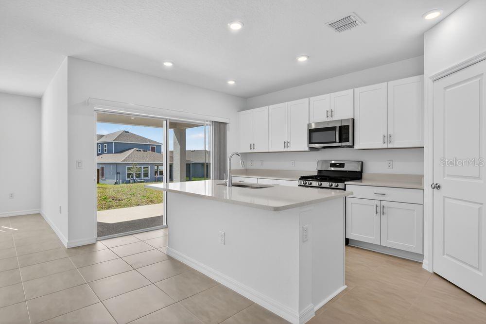 A modern kitchen features white cabinets, a central island with a sink, and sliding glass doors — 217 STREAMWATER WAY, GROVELAND, FL