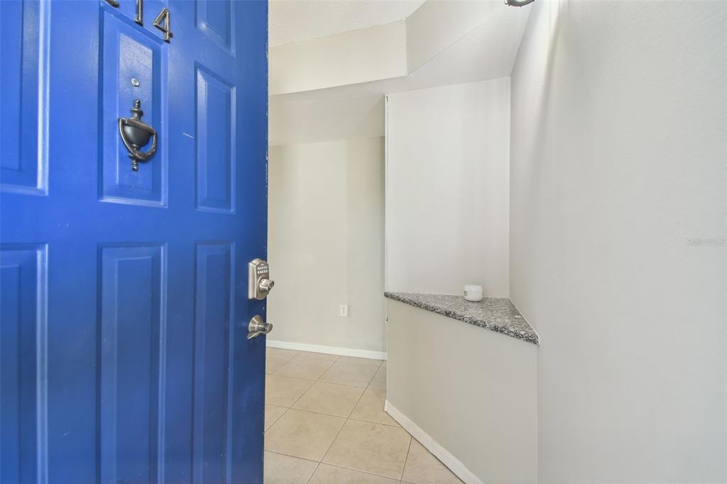 An open blue front door reveals a tiled entryway with a granite-topped corner shelf — 5557 SEA FOREST DRIVE UNIT 214, NEW PORT RICHEY, FL
