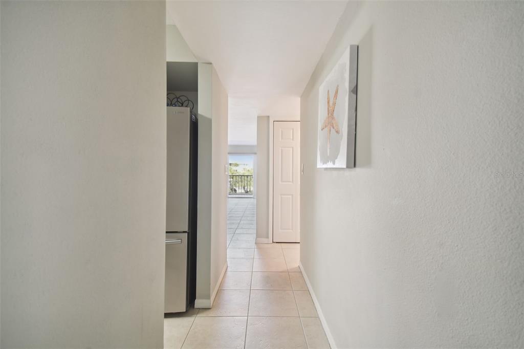 A hallway with light tile flooring leads toward a balcony with an outdoor view — 5557 SEA FOREST DRIVE UNIT 214, NEW PORT RICHEY, FL