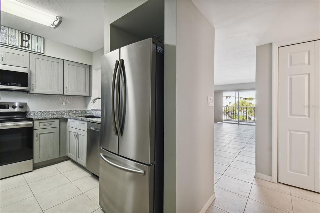 A kitchen with stainless steel appliances and grey cabinets opens into a tiled living area — 5557 SEA FOREST DRIVE UNIT 214, NEW PORT RICHEY, FL