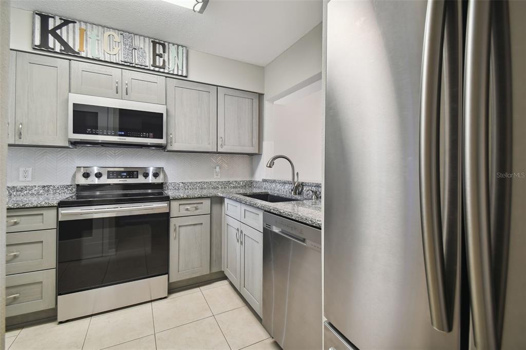 A kitchen features light gray cabinets, stainless steel appliances, and granite countertops — 5557 SEA FOREST DRIVE UNIT 214, NEW PORT RICHEY, FL