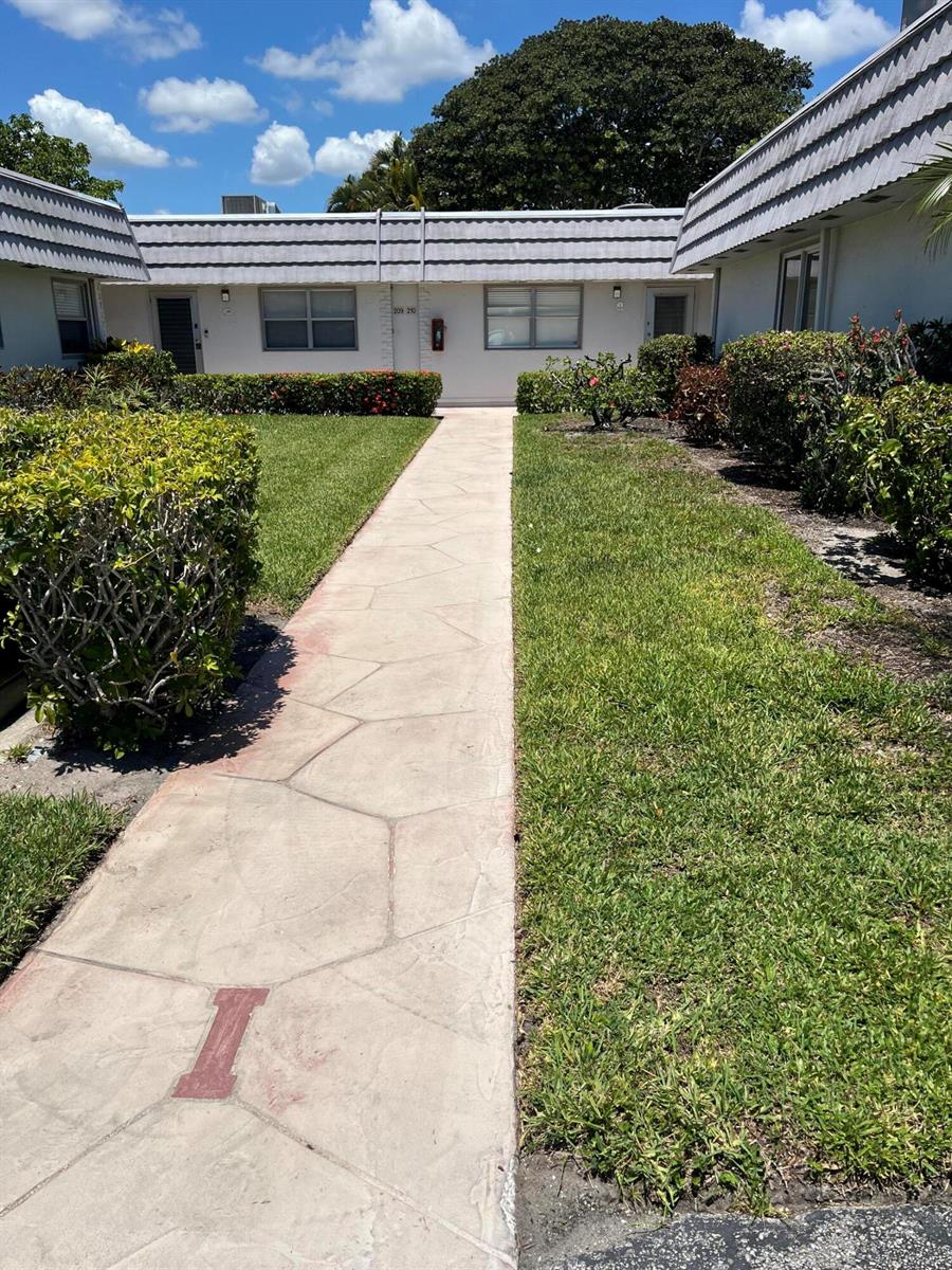 A concrete walkway leads to the entrance of a single-story residential building with landscaping — 210 Valencia I, Delray Beach FL 33446, DELRAY BEACH, FL