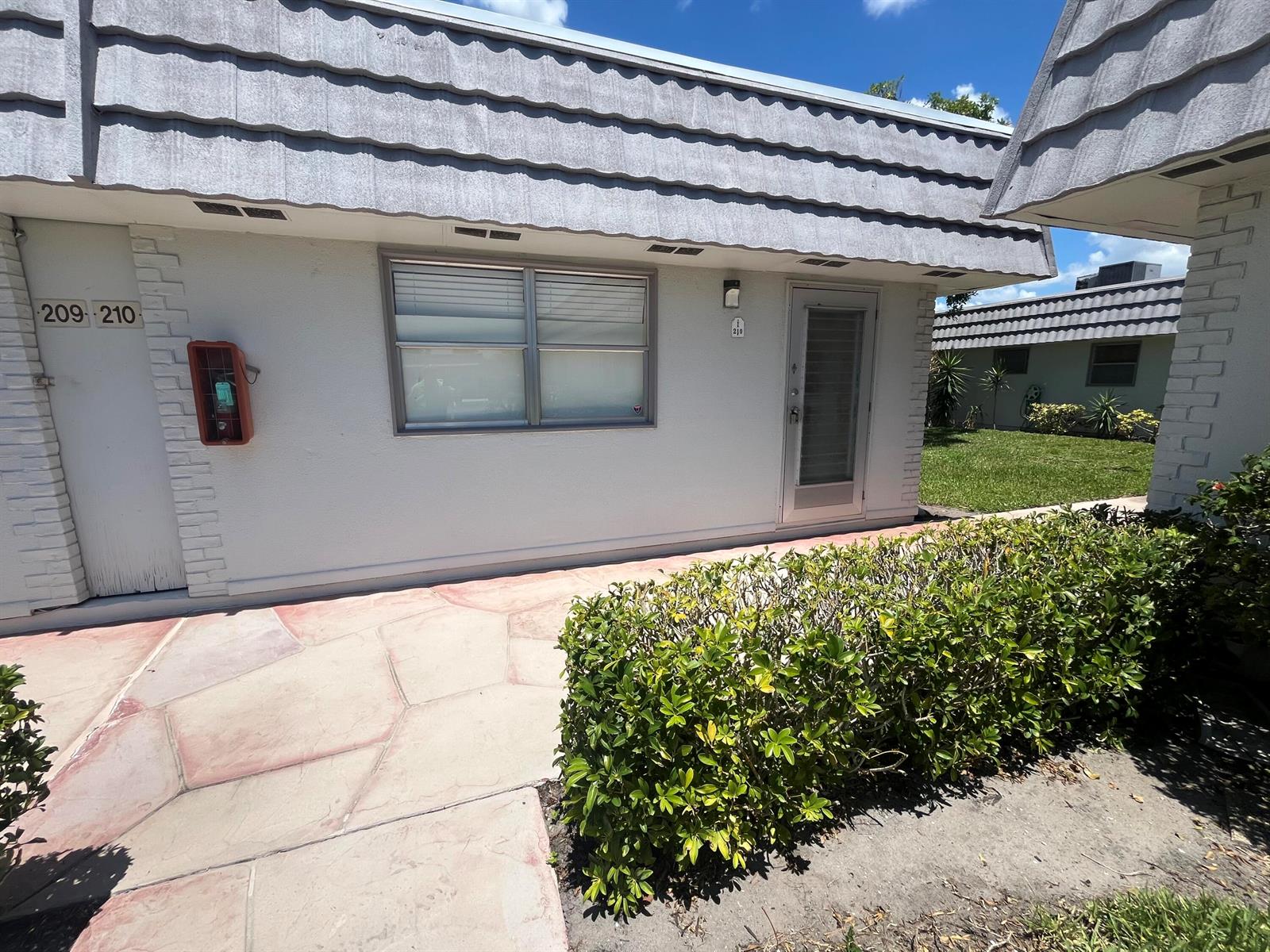 Exterior view of a single-story building with a gray tiled roof and white walls — 210 Valencia I, Delray Beach FL 33446, DELRAY BEACH, FL