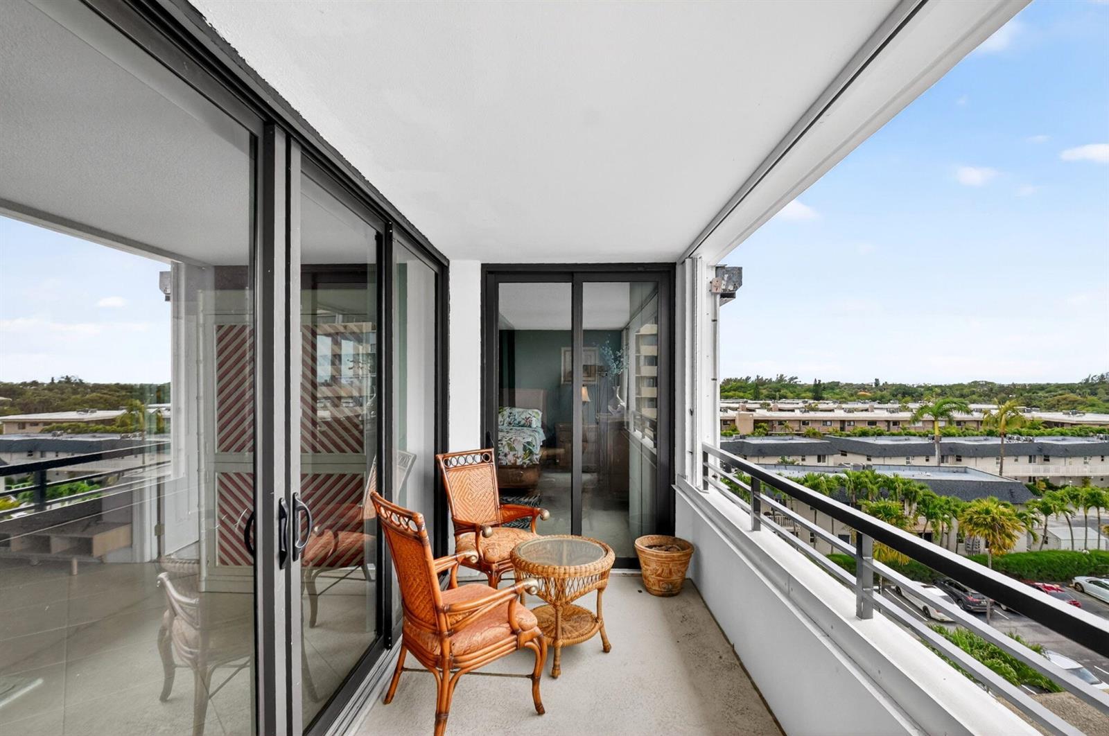 A balcony with wicker furniture overlooks a residential neighborhood with palm trees and buildings — 3589 S Ocean Boulevard # 609, South Palm Beach FL 33480, SOUTH PALM BEACH, FL