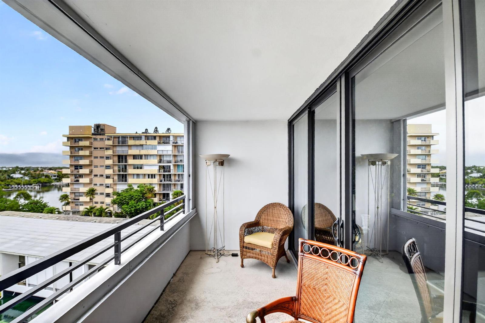 A balcony with wicker chairs, a floor lamp, and views of a neighboring apartment building — 3589 S Ocean Boulevard # 609, South Palm Beach FL 33480, SOUTH PALM BEACH, FL
