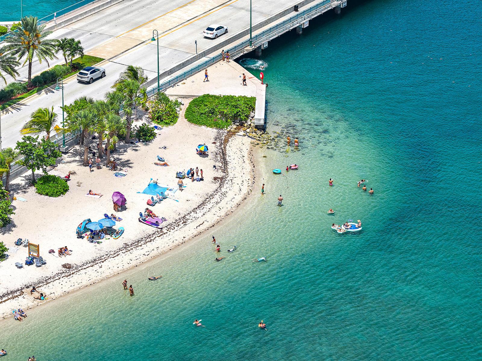 An aerial view shows a sandy beach with people swimming and relaxing near a bridge — 176 E 24th Street, Riviera Beach FL 33404, RIVIERA BEACH, FL