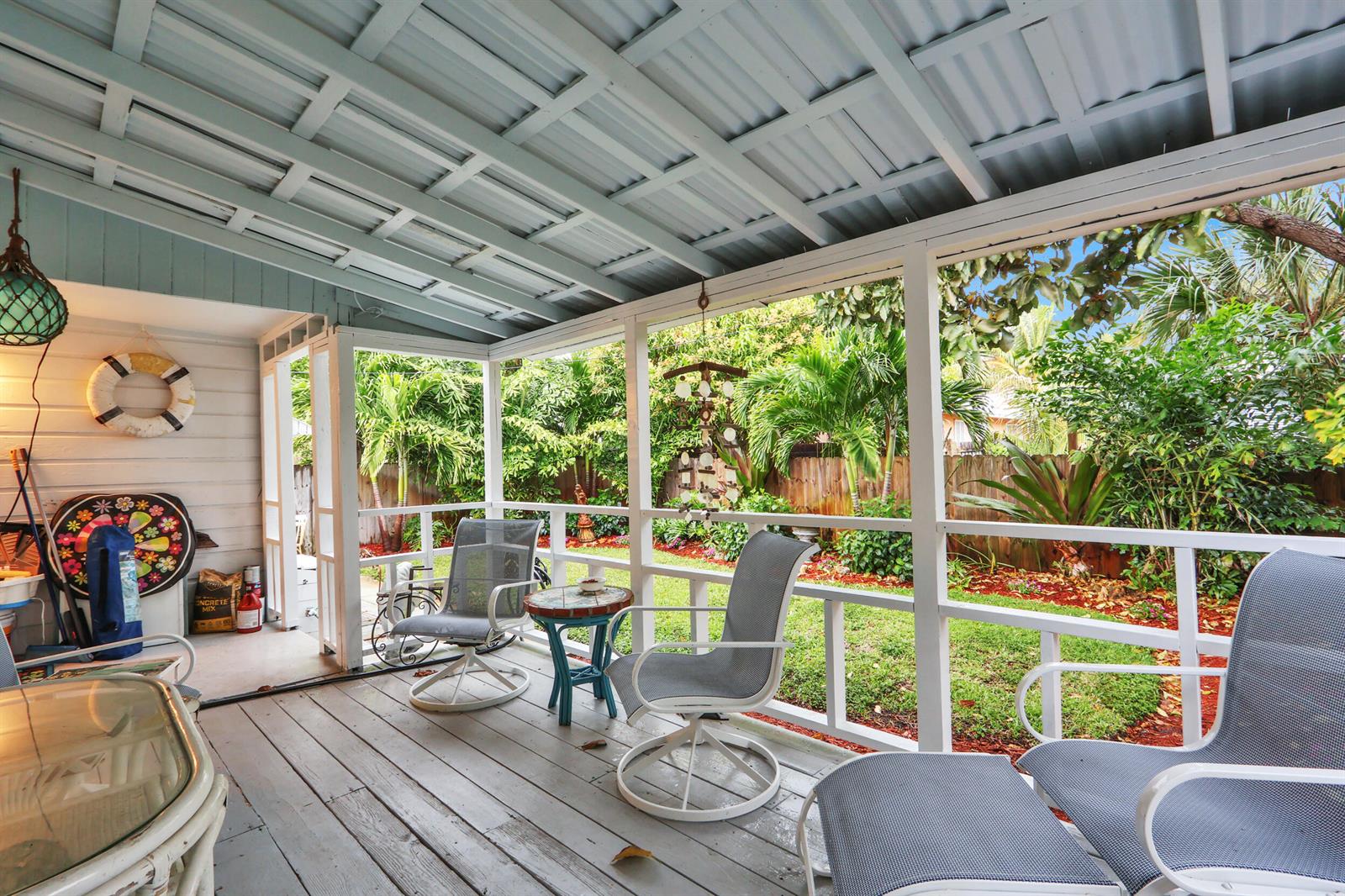 A screened-in porch with a wooden floor, white railings, and outdoor furniture overlooking a yard — 176 E 24th Street, Riviera Beach FL 33404, RIVIERA BEACH, FL