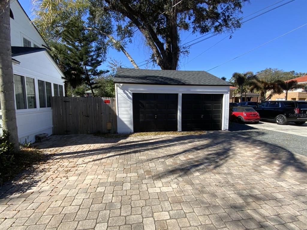 A white detached two-car garage with black doors sits behind a house with a paver driveway — 608 HIGHLAND AVENUE, ORLANDO, FL