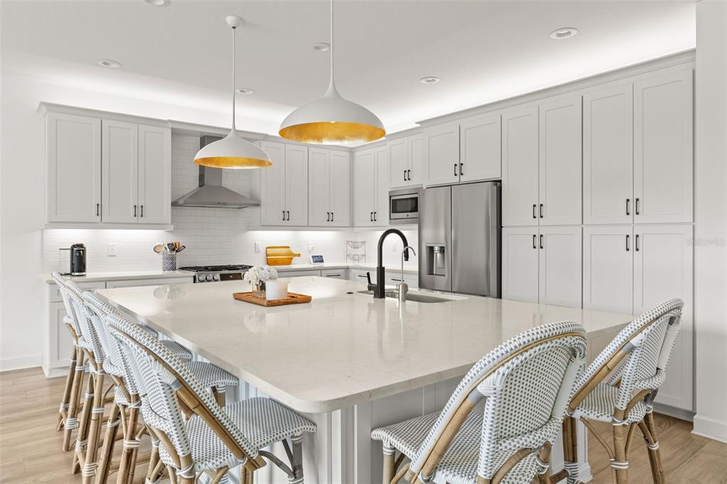 A modern kitchen features white cabinetry, a large quartz island, and woven bar stools — 3541 GREAT BANYAN WAY, WESLEY CHAPEL, FL