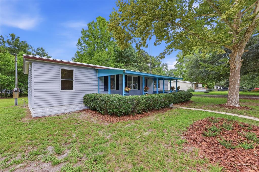 A light blue single-story house with a covered front porch and a large shade tree — 187 SW PEACH GLEN, HIGH SPRINGS, FL