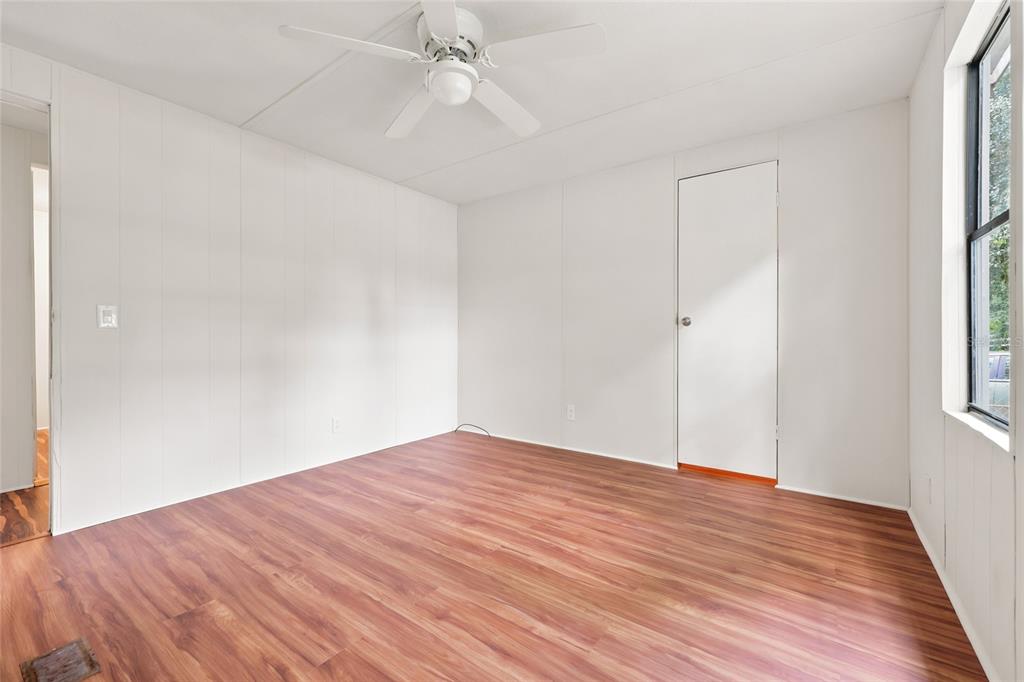 An empty bedroom with white paneled walls, wood-look flooring, a ceiling fan, and a closet — 187 SW PEACH GLEN, HIGH SPRINGS, FL