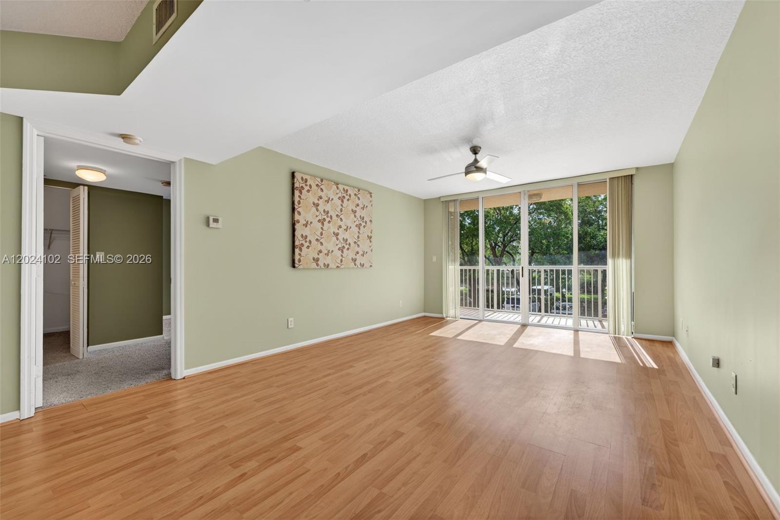 This living room features light green walls, wood-look flooring, a ceiling fan, and a balcony — 619 E Sheridan St # 203, Dania Beach FL 33004, DANIA BEACH, FL