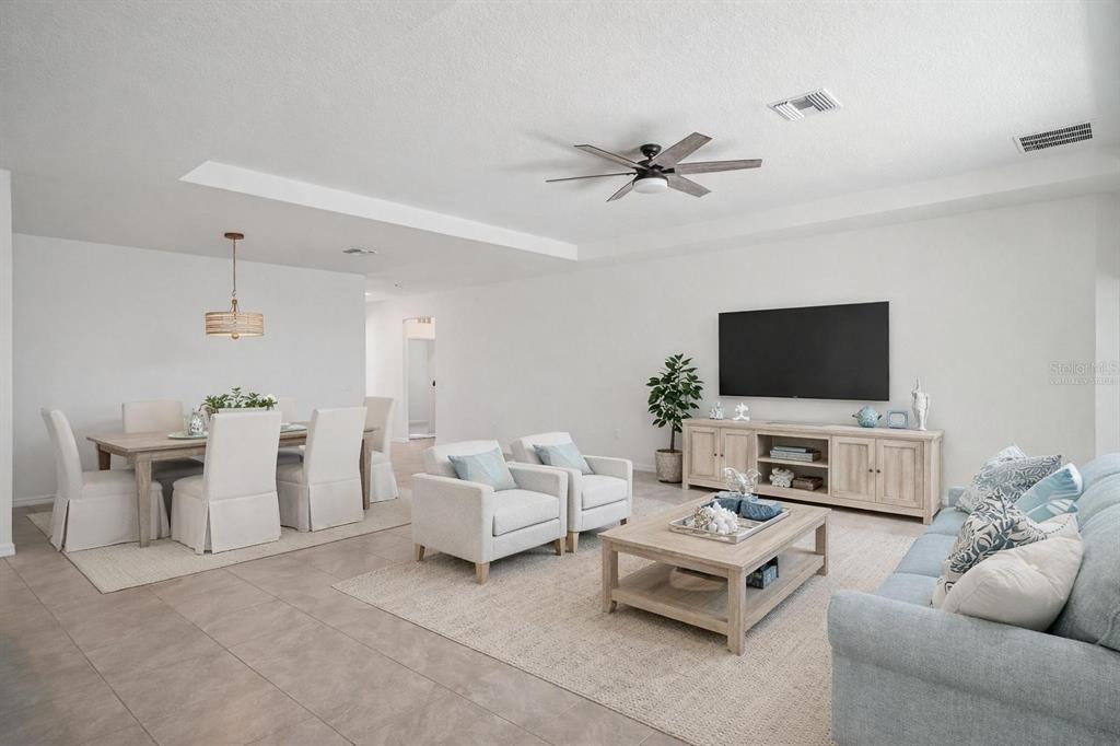 An open-concept living and dining area features light-colored furniture, tile flooring, and a ceiling fan — 3458 AUTUMN AMBER DR, SPRING HILL, FL