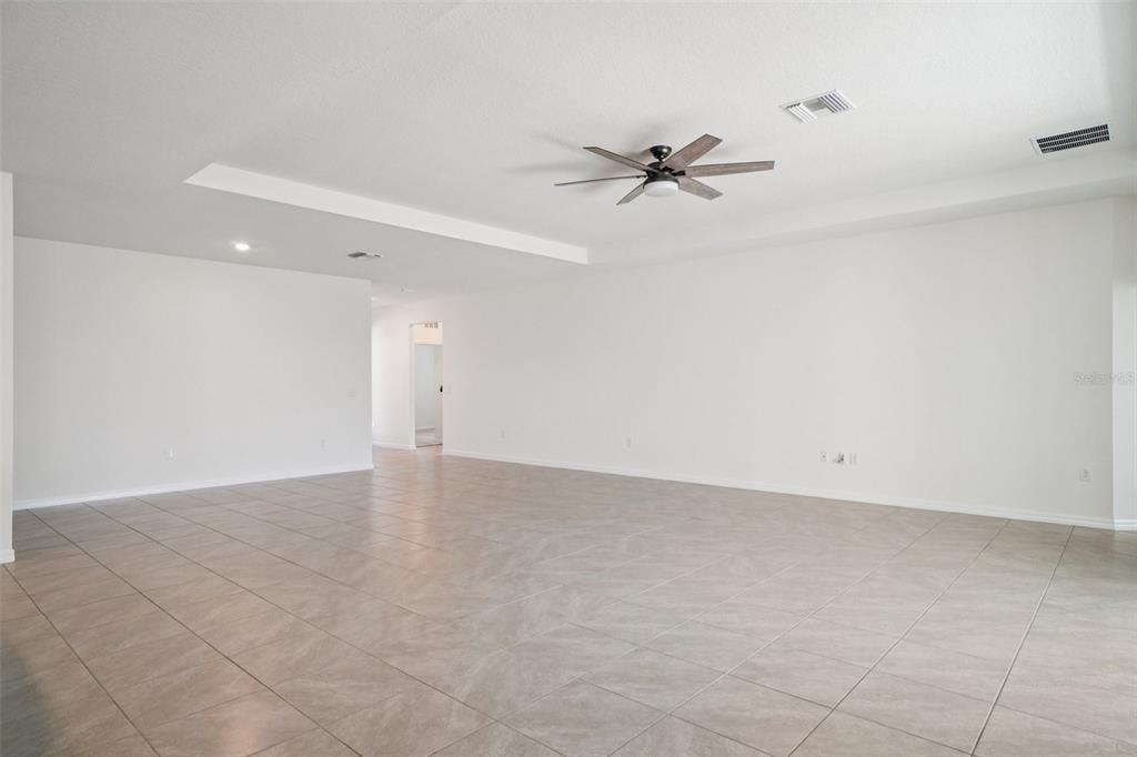 A spacious, empty room features white walls, light-colored tile flooring, and a ceiling fan — 3458 AUTUMN AMBER DR, SPRING HILL, FL
