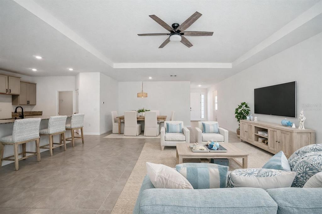 An open-concept living and dining area features tile flooring, a ceiling fan, and neutral furniture — 3458 AUTUMN AMBER DR, SPRING HILL, FL