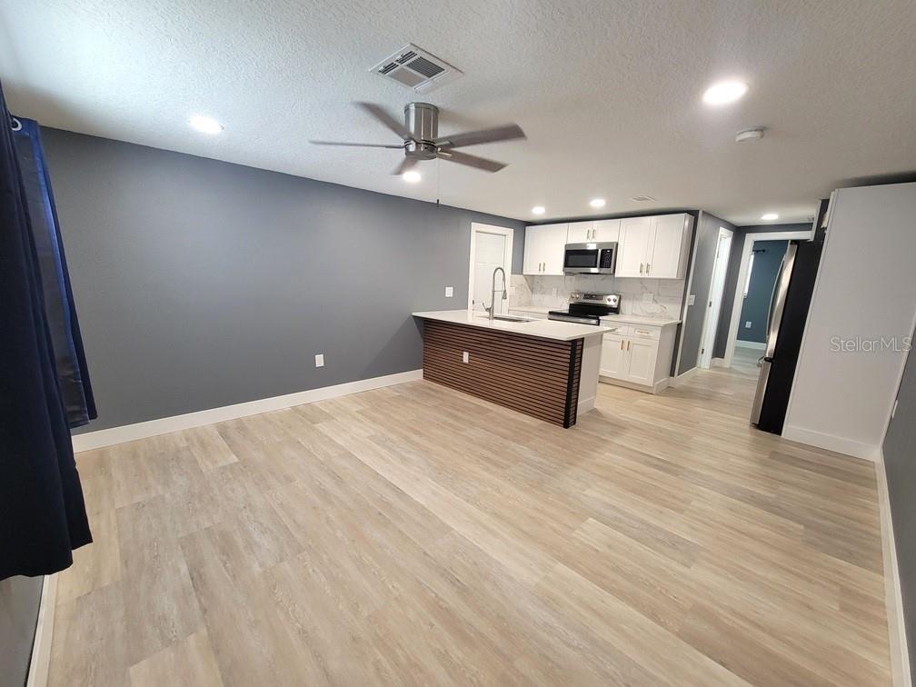 An open-concept kitchen features white cabinets, a slatted island, and light wood-look flooring — 4944 ELKNER STREET, NEW PORT RICHEY, FL