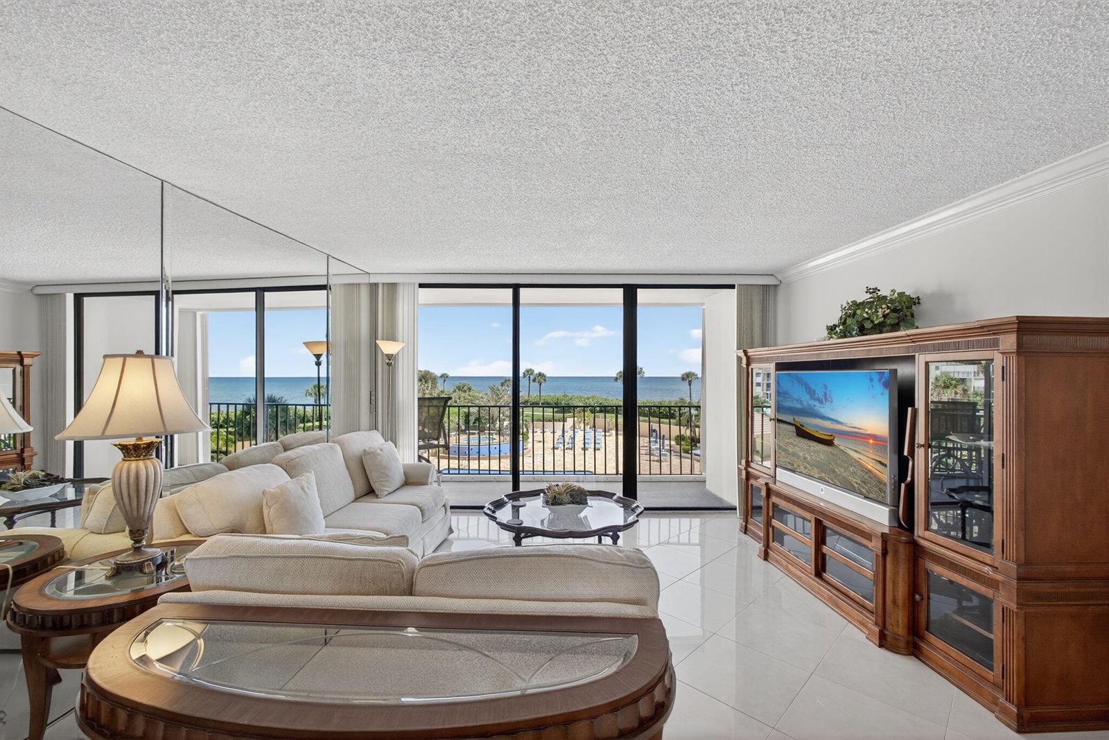 A living room with white tile floors, a beige sofa, and a balcony overlooking the ocean — 100 Ocean Trail Way # 305, Jupiter FL 33477, JUPITER, FL