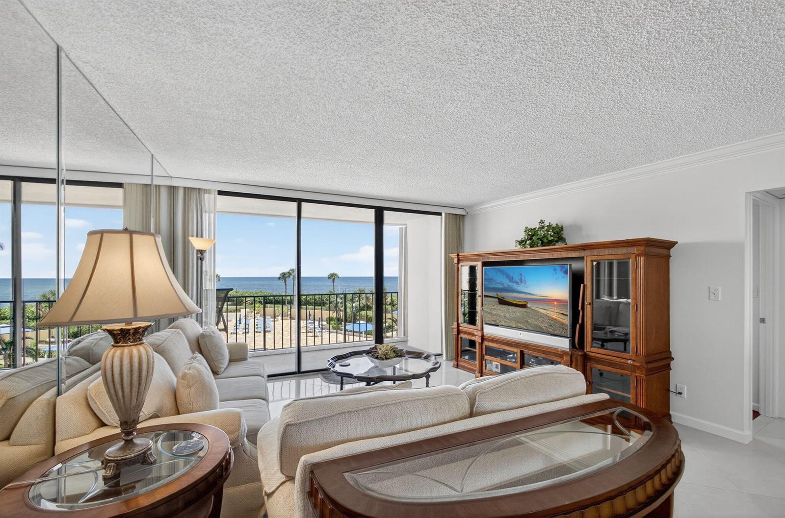 A living room features a beige sofa, wooden entertainment center, and a balcony overlooking the ocean — 100 Ocean Trail Way # 305, Jupiter FL 33477, JUPITER, FL