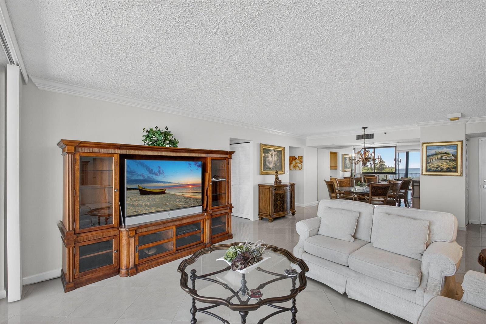 A living room with a large wooden entertainment center, glass coffee table, and white sofa — 100 Ocean Trail Way # 305, Jupiter FL 33477, JUPITER, FL