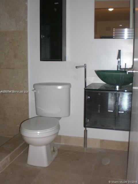 A bathroom features a white toilet, a glass vessel sink, and a dark vanity cabinet — 577 NE 62 STREET # 2, Miami FL 33138, MIAMI, FL