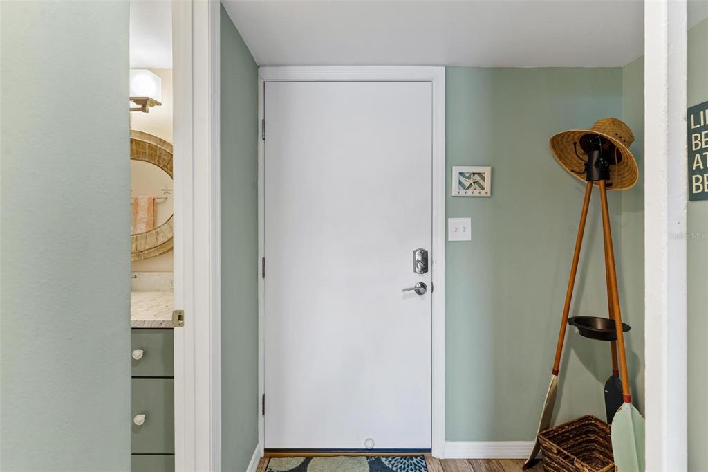 An entryway features a white door, a coat rack with a hat, and a nearby bathroom — 4841 SAXON DRIVE UNIT E206, NEW SMYRNA BEACH, FL