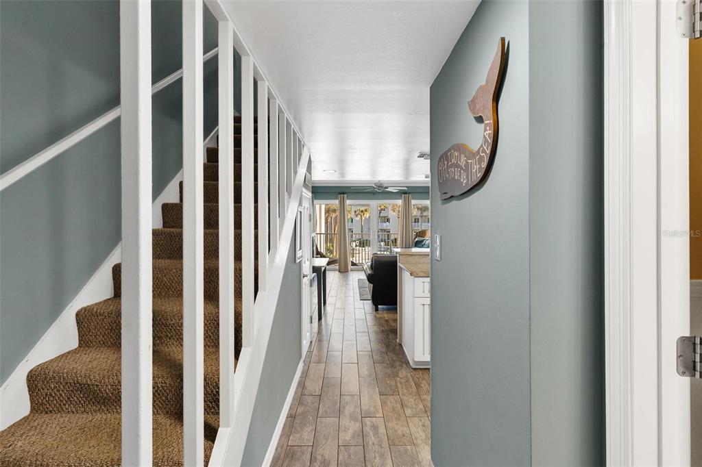 A hallway with a carpeted staircase and wood-look tile flooring leads toward an open living area — 4841 SAXON DRIVE UNIT E206, NEW SMYRNA BEACH, FL