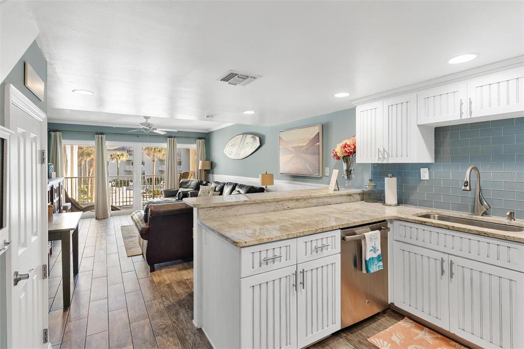 A kitchen with white cabinets and granite countertops overlooks a living area with balcony access — 4841 SAXON DRIVE UNIT E206, NEW SMYRNA BEACH, FL