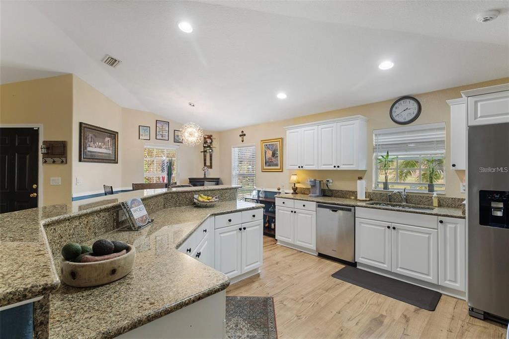 A kitchen features white cabinets, granite countertops, stainless steel appliances, and light wood flooring — 3953 VEHLIN STREET, NORTH PORT, FL
