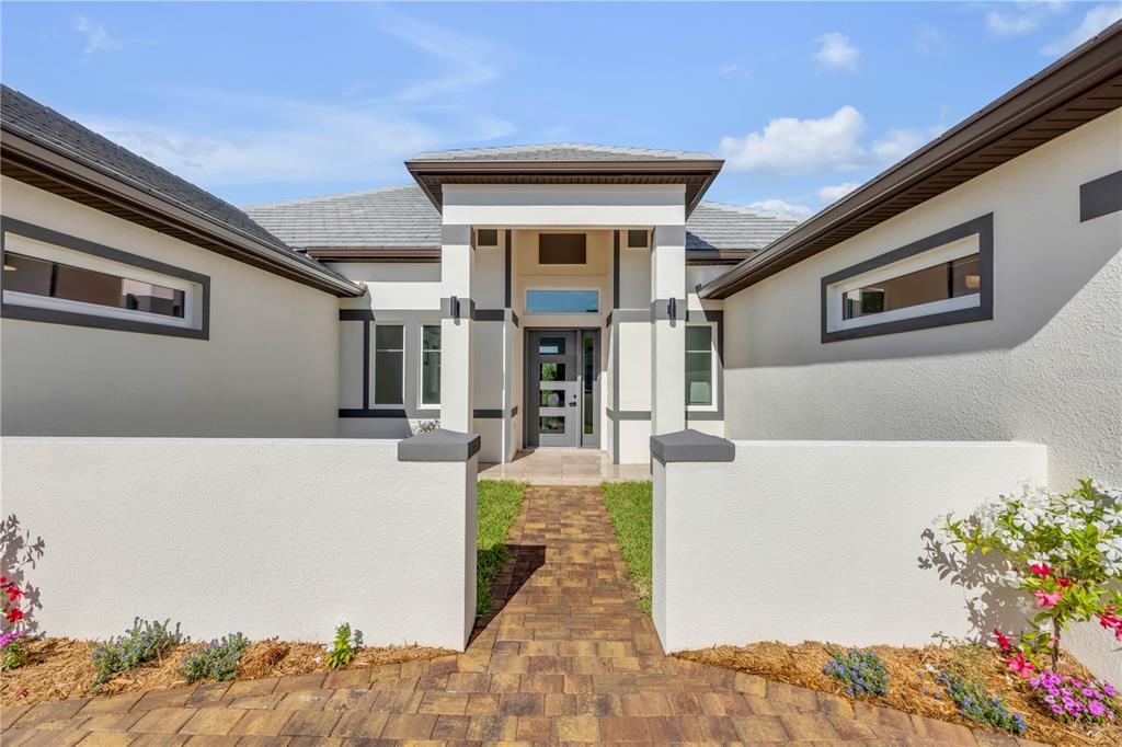 A paved walkway leads to the front entrance of a modern house with white walls — 116 LONGVIEW WAY N, PALM COAST, FL