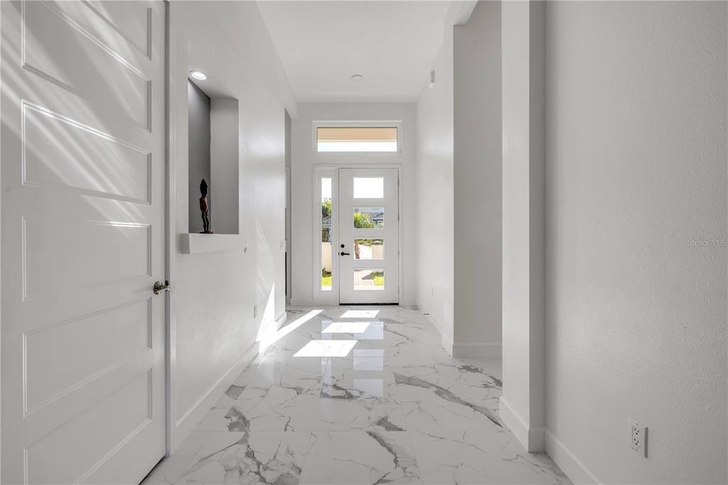 A bright entryway features white walls, marble-look tile flooring, and a modern glass-paneled front door — 116 LONGVIEW WAY N, PALM COAST, FL