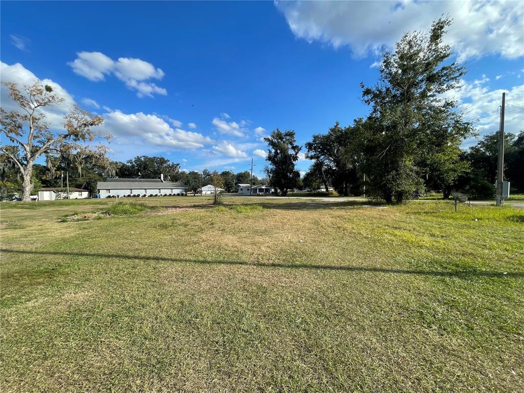 A wide, grassy vacant lot under a blue sky with scattered trees and distant buildings — 7 4TH STREET SE, FORT MEADE, FL