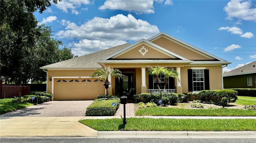 A single-story suburban house with a tan stucco exterior, a two-car garage, and landscaping — 1801 BURDOCK DRIVE, WINTER GARDEN, FL