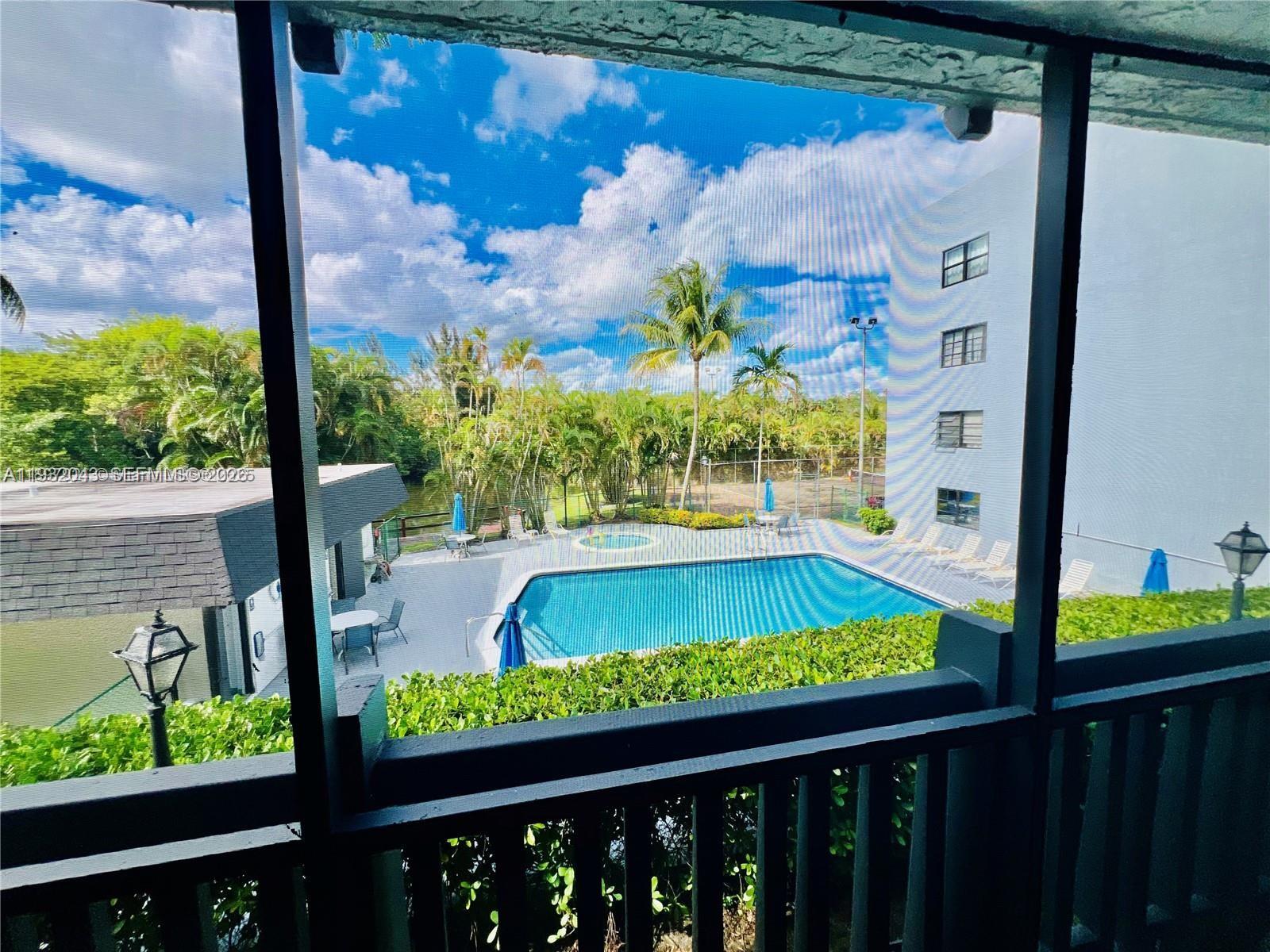 A view of a swimming pool and surrounding landscaping from a screened-in balcony — 1021 Mockingbird Ln # 215, Plantation FL 33324, PLANTATION, FL