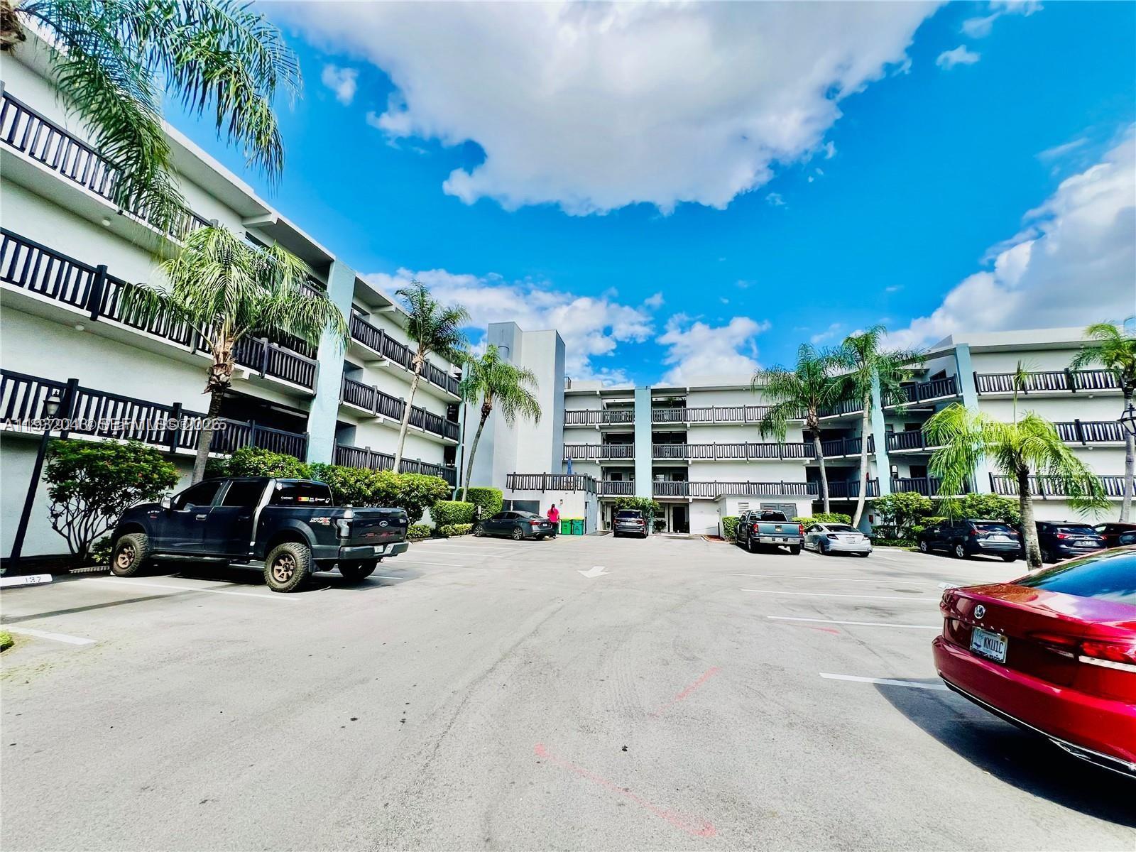A parking lot sits in front of a multi-story apartment building with exterior balconies — 1021 Mockingbird Ln # 215, Plantation FL 33324, PLANTATION, FL