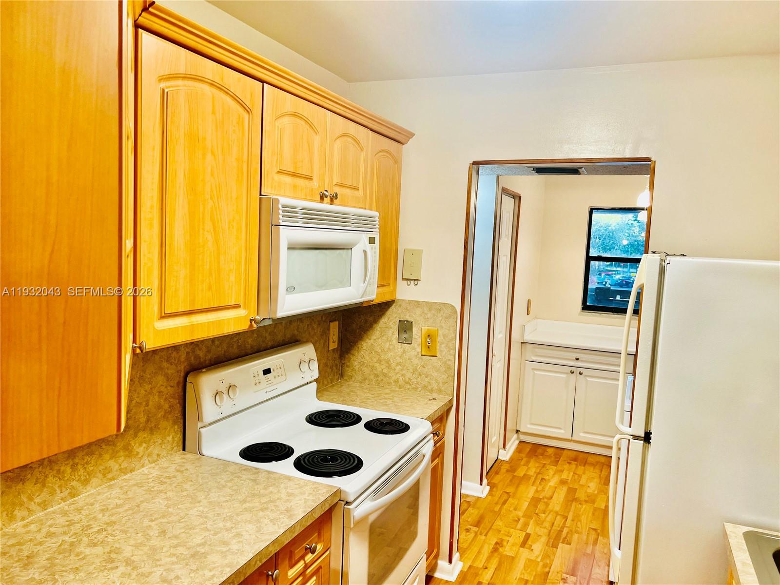 A kitchen features light wood cabinets, white appliances, laminate countertops, and a doorway to another room — 1021 Mockingbird Ln # 215, Plantation FL 33324, PLANTATION, FL