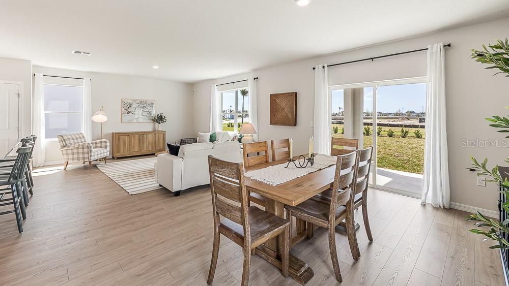 An open-concept living and dining area features wood-look flooring, a sliding glass door, and furniture — 18705 LOOKOUT RIDGE PLACE, LAKEWOOD RANCH, FL