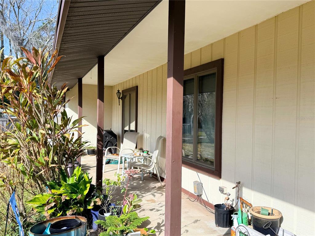A covered porch with vertical siding, brown support posts, and several potted plants — 1627 DECATUR AVENUE, HOLLY HILL, FL
