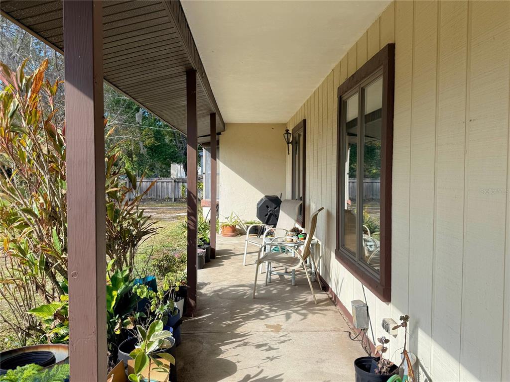 A covered concrete porch features potted plants, outdoor chairs, and a grill along the house — 1627 DECATUR AVENUE, HOLLY HILL, FL