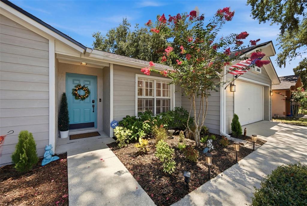 A light gray house with a teal front door, a blooming tree, and a garage — 2409 ARBORWOOD DRIVE, VALRICO, FL