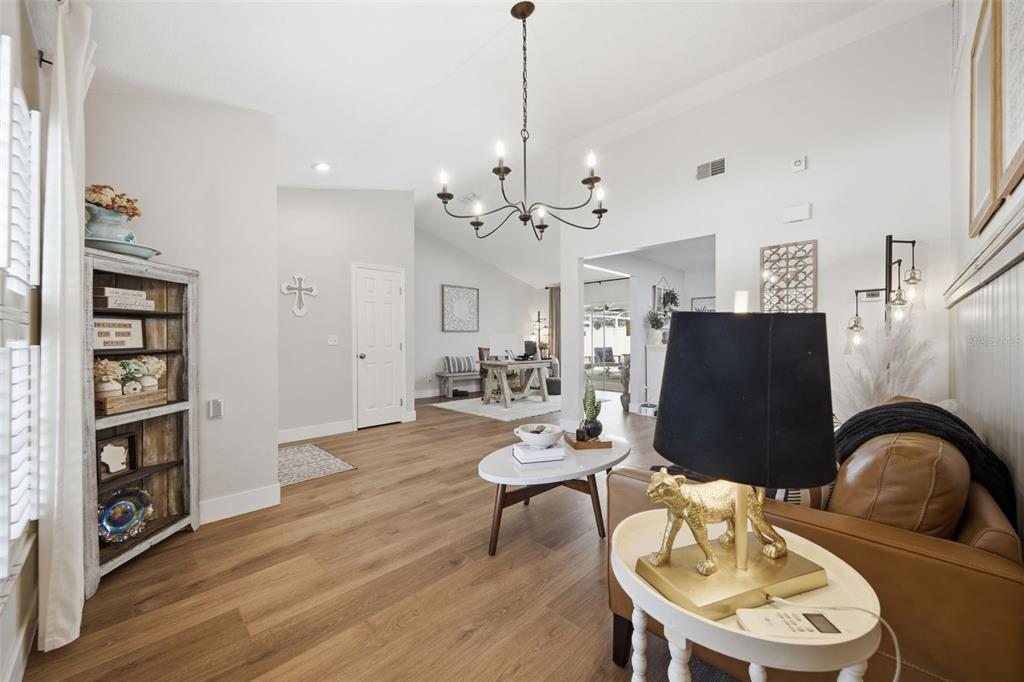 A bright living room features wood-look flooring, a chandelier, and a leather sofa — 2409 ARBORWOOD DRIVE, VALRICO, FL