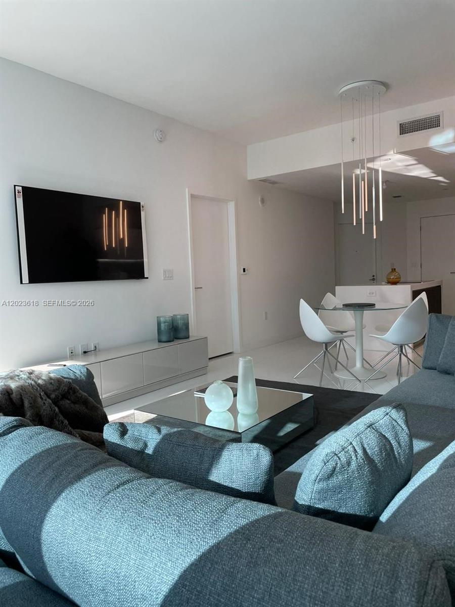 A modern living room features a grey sectional sofa, a television, and a dining area — 851 NE 1st Ave # 1006, Miami FL 33132, MIAMI, FL