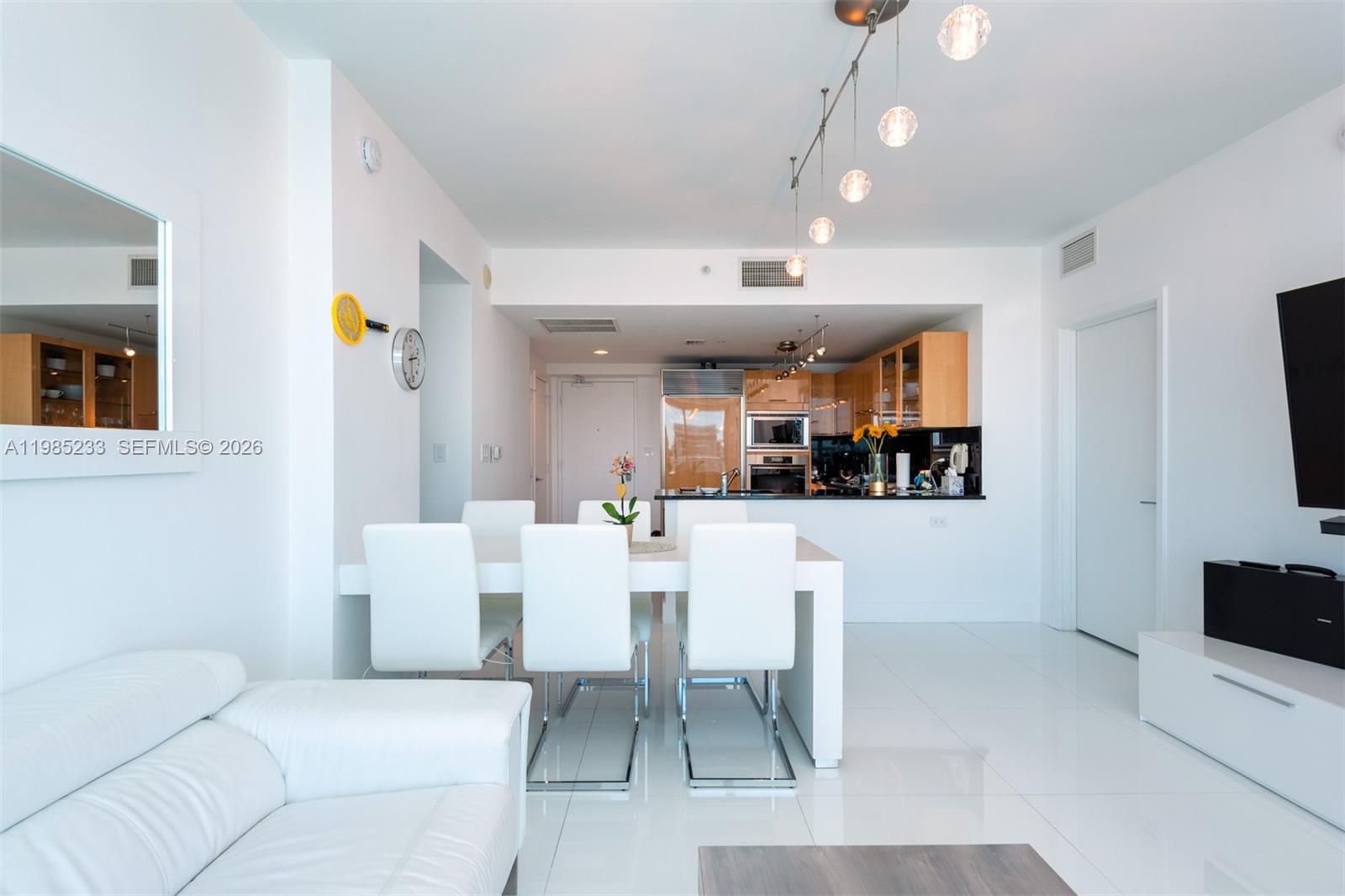 A modern open-concept living and dining area features white tile floors and minimalist furniture — 6799 Collins Ave # 906, Miami Beach FL 33141, MIAMI BEACH, FL