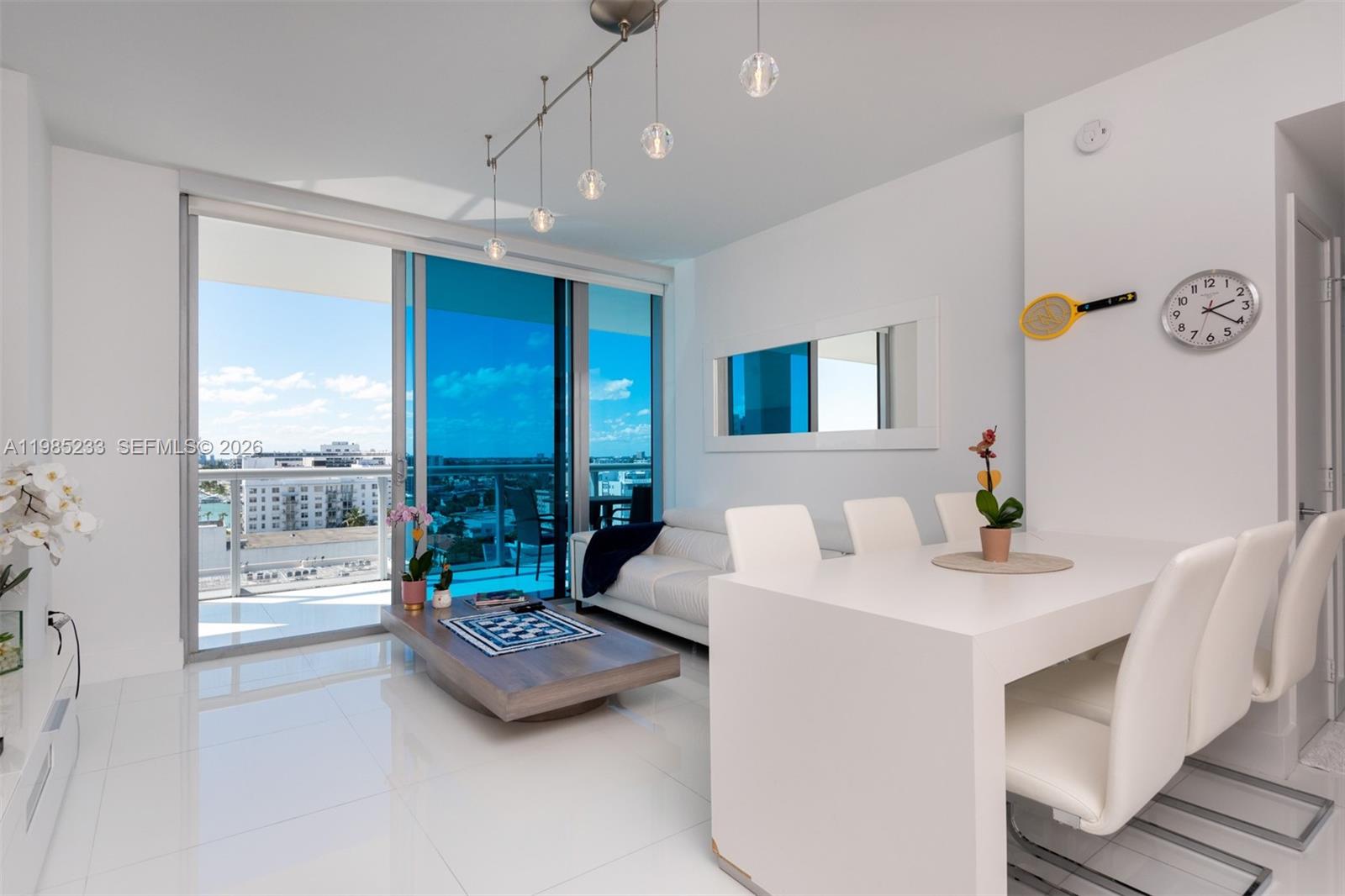 A modern living and dining area with white tile floors, floor-to-ceiling windows, and balcony views — 6799 Collins Ave # 906, Miami Beach FL 33141, MIAMI BEACH, FL